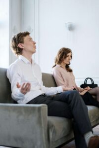 Couple sitting on couch receiving marriage therapy. One partner is frustrated. 