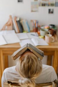 Person sitting in chair with head tilted back and open book laying on to of head feeling overwhelmed with election anxiety. 