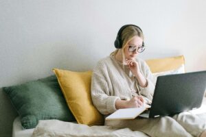 Person sitting in bed using headphones and a note book to mentally and emotionally prepare for online therapy appointment. 