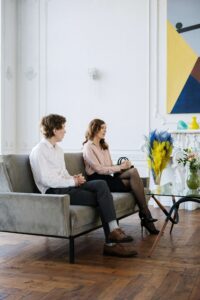 Couples sitting on couch as they attend couples counseling both seem to have distant expresseions