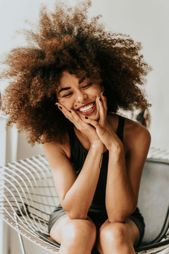 Person smiling while holding face with excitement about their self-discovery and embodiment.