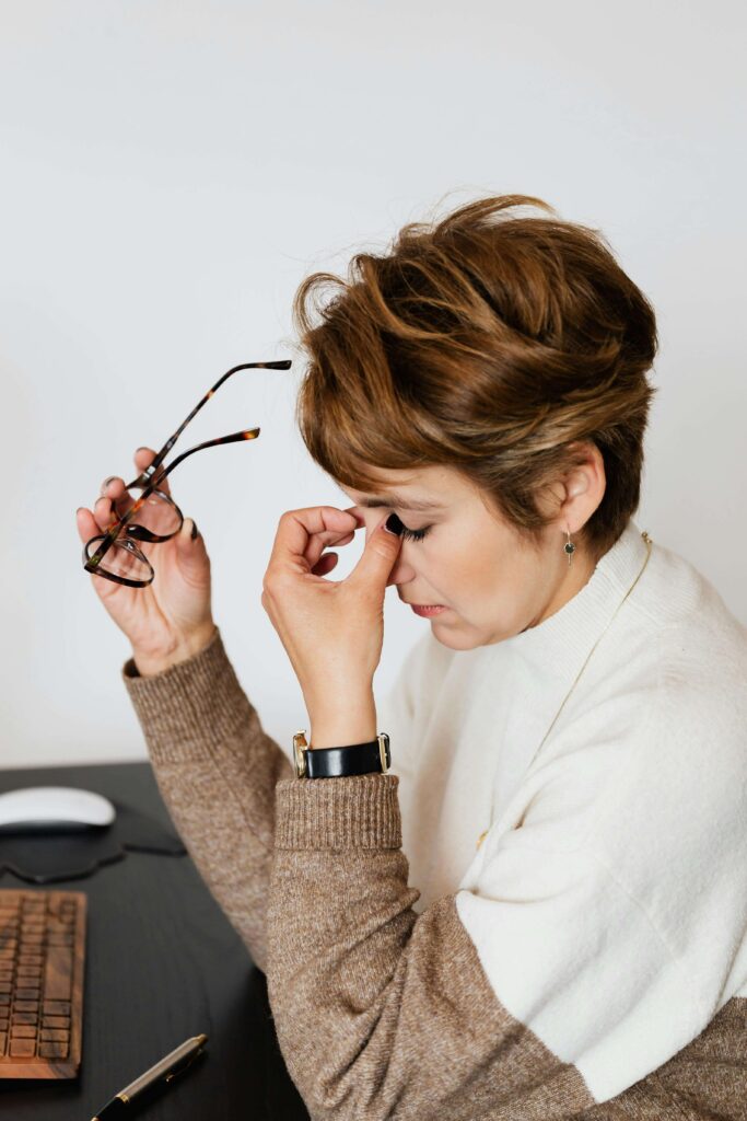 Person sitting down with fingers pinching bridge of nose due to stress, overwhelm and guilt.