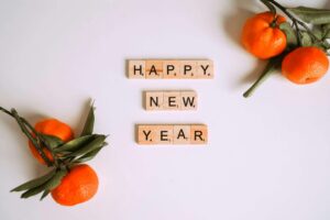 A few oranges on a table with scrabble letters in the center saying "Happy New Year"