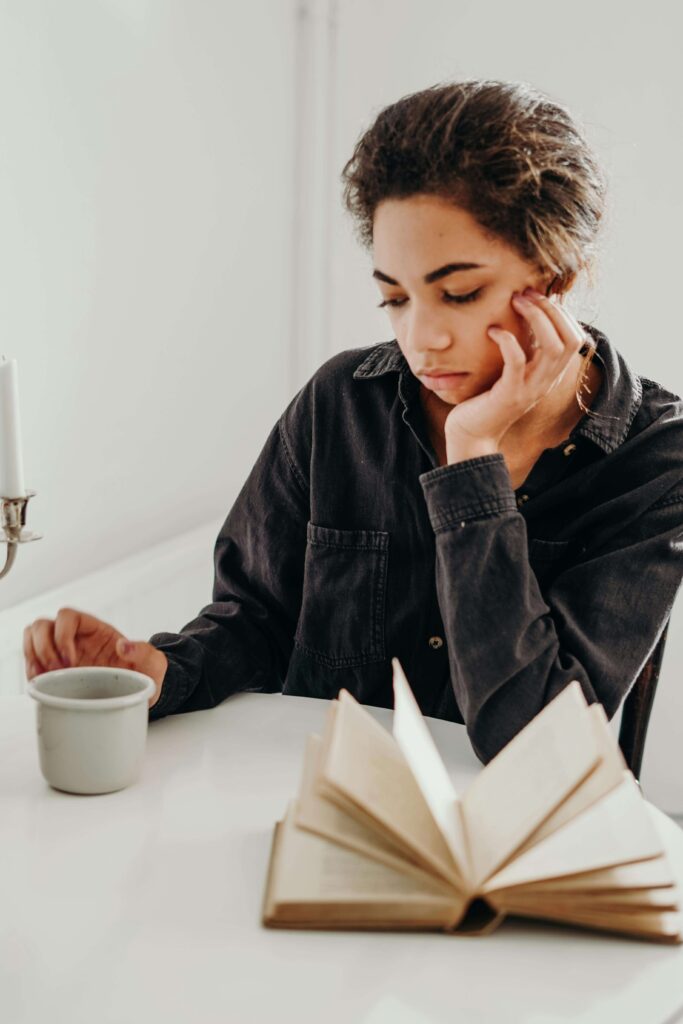 Person siting at table resting their chin in hand and staring down at their cup looking disheartened and tired.