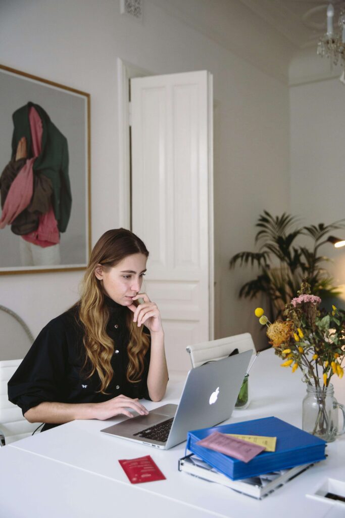 Person on a computer at a table with books, notes and stacks of items as they are productive to distract from anxiety and panic they feel.