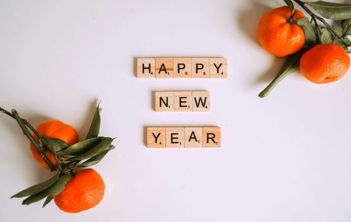 A few oranges on a table with scrabble letters in the center saying "Happy New Year"