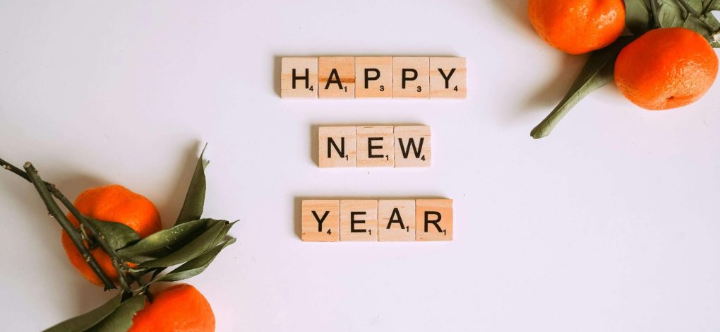 A few oranges on a table with scrabble letters in the center saying "Happy New Year"